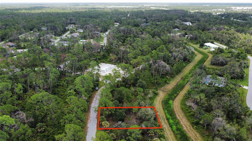 An aerial view shows a rectangular vacant lot outlined in red amidst a wooded area — APRICOLA RD, NORTH PORT, FL