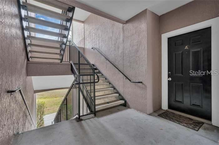 An outdoor stairwell leads to a black front door of a residential unit — 3446 SOHO STREET UNIT 104, ORLANDO, FL