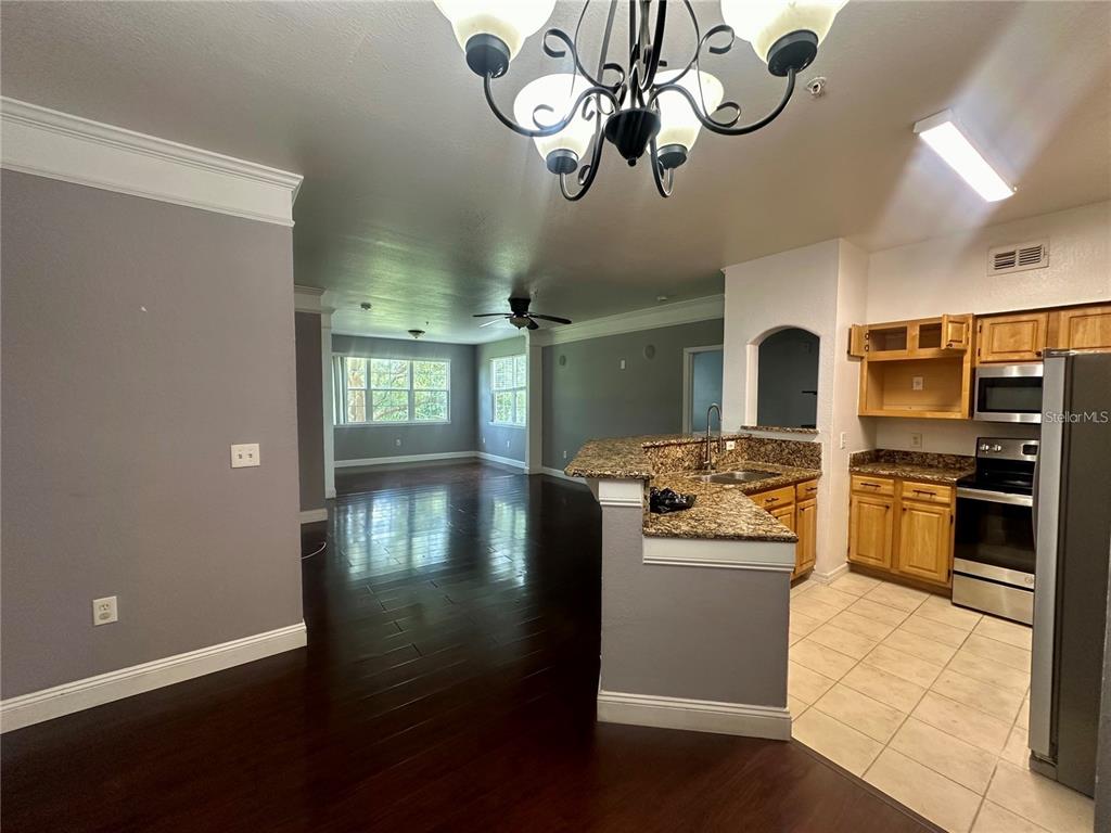 An open-concept kitchen with granite countertops and wood cabinets overlooks a dark-floored living area — 3446 SOHO STREET UNIT 104, ORLANDO, FL