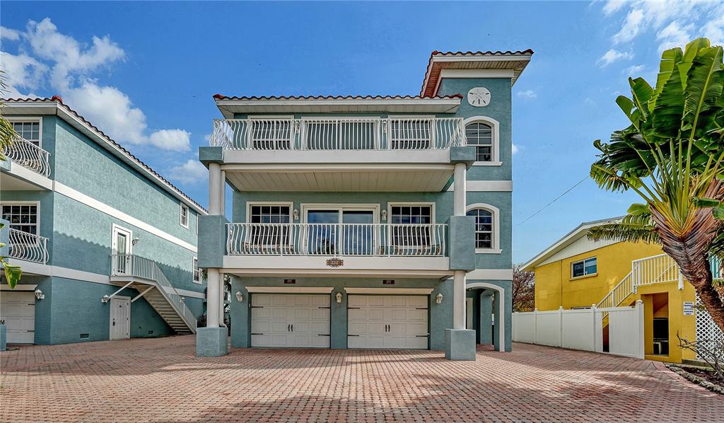 A three-story teal house with two garage doors and balconies sits on a brick driveway — 2317 AVENUE C UNIT 300, BRADENTON BEACH, FL