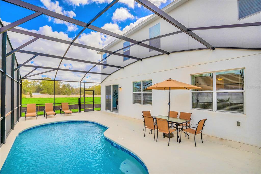 A swimming pool with a screened enclosure and a patio dining set outside a house — 4481 MONADO DRIVE, KISSIMMEE, FL