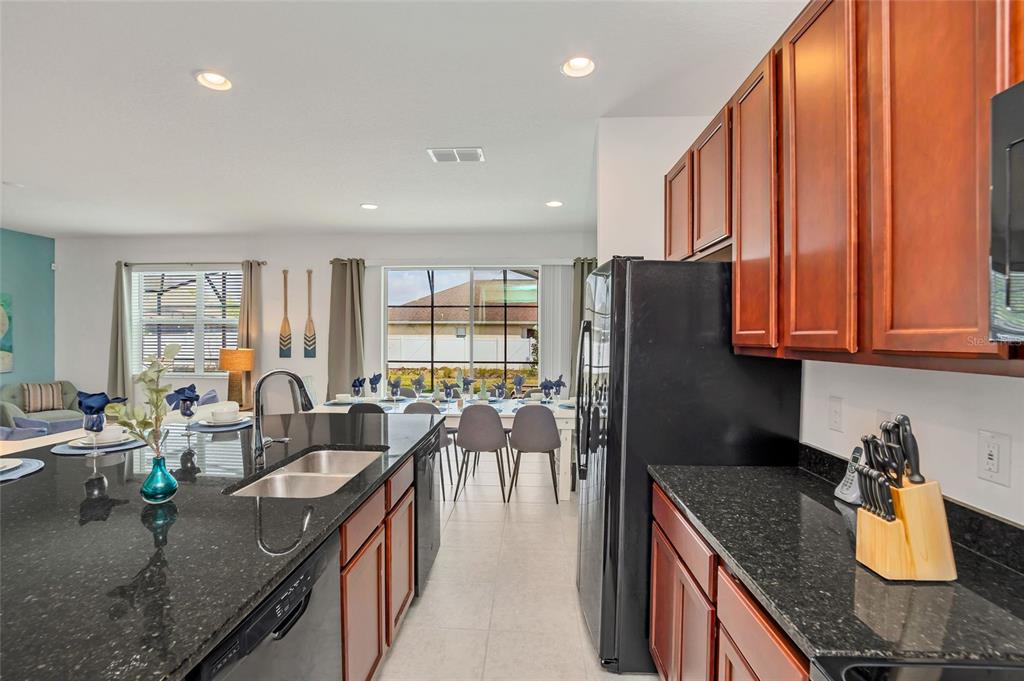 A kitchen with dark granite countertops and wood cabinets overlooks a dining area and living room — 4481 MONADO DRIVE, KISSIMMEE, FL