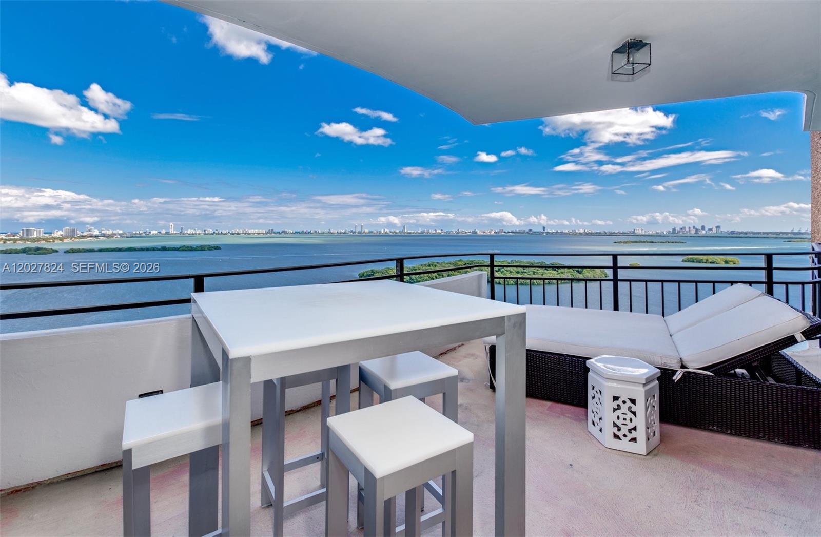 A balcony features a metal dining set, a lounge chair, and a panoramic water view — 720 NE 69th St # 19S, Miami FL 33138, MIAMI, FL