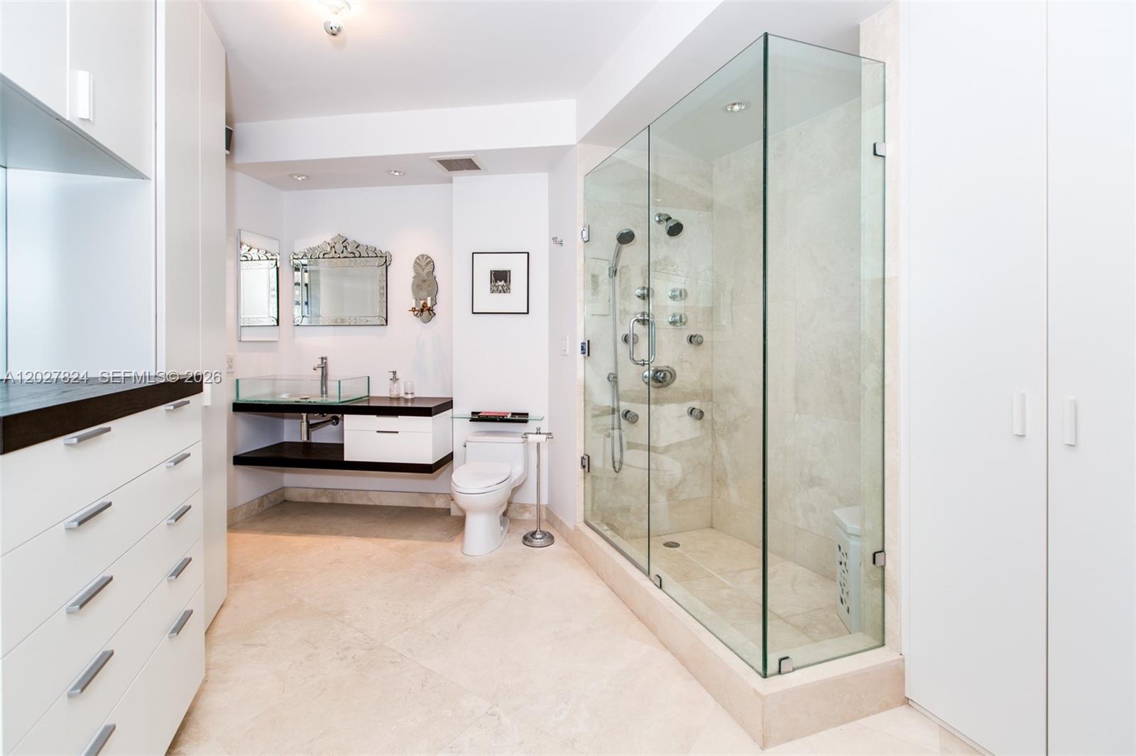 A modern bathroom features a glass-enclosed shower, a floating vanity, and light-colored tile flooring — 720 NE 69th St # 19S, Miami FL 33138, MIAMI, FL