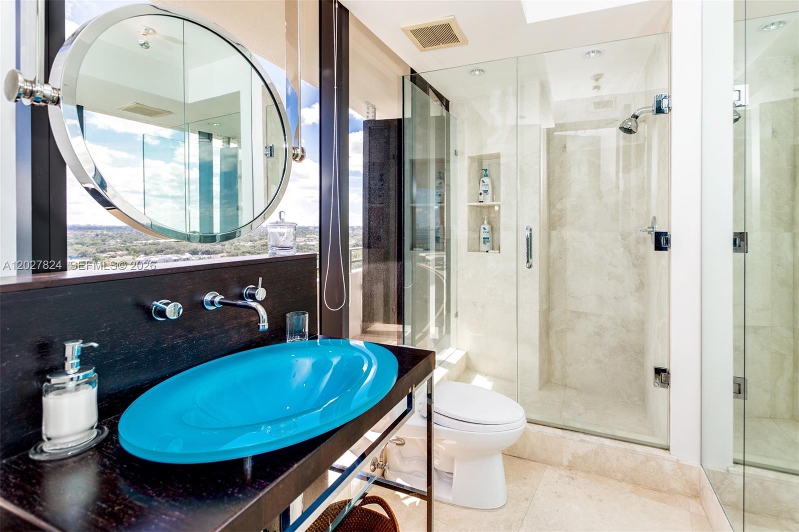 A bathroom features a blue glass vessel sink, a walk-in shower, and a round mirror — 720 NE 69th St # 19S, Miami FL 33138, MIAMI, FL