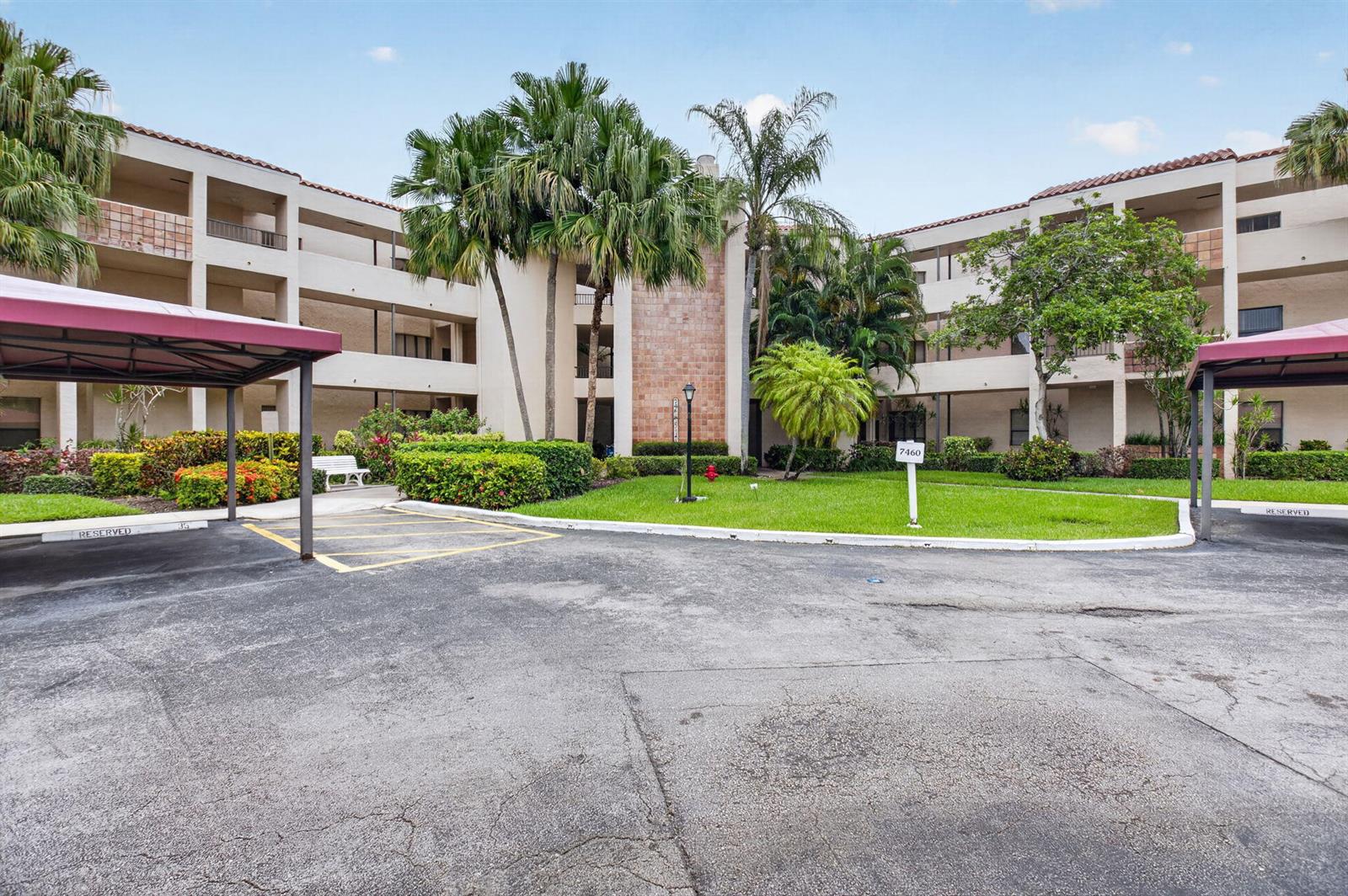 An exterior view of a multi-story apartment building with covered parking and landscaped grounds — 7460 La Paz Boulevard # 306, Boca Raton FL 33433, BOCA RATON, FL