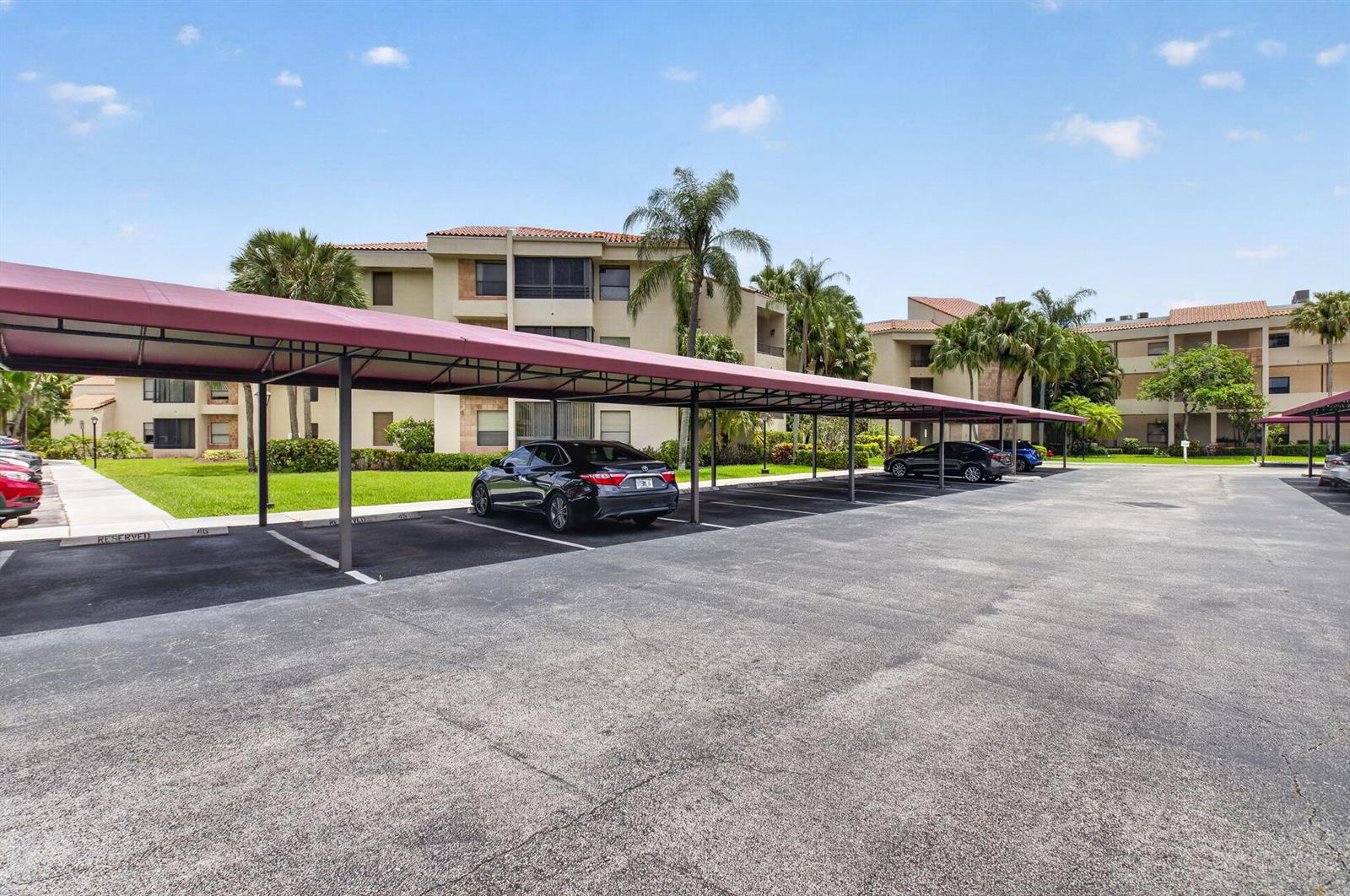 A parking lot features a long, covered carport structure in front of a multi-story apartment building — 7460 La Paz Boulevard # 306, Boca Raton FL 33433, BOCA RATON, FL