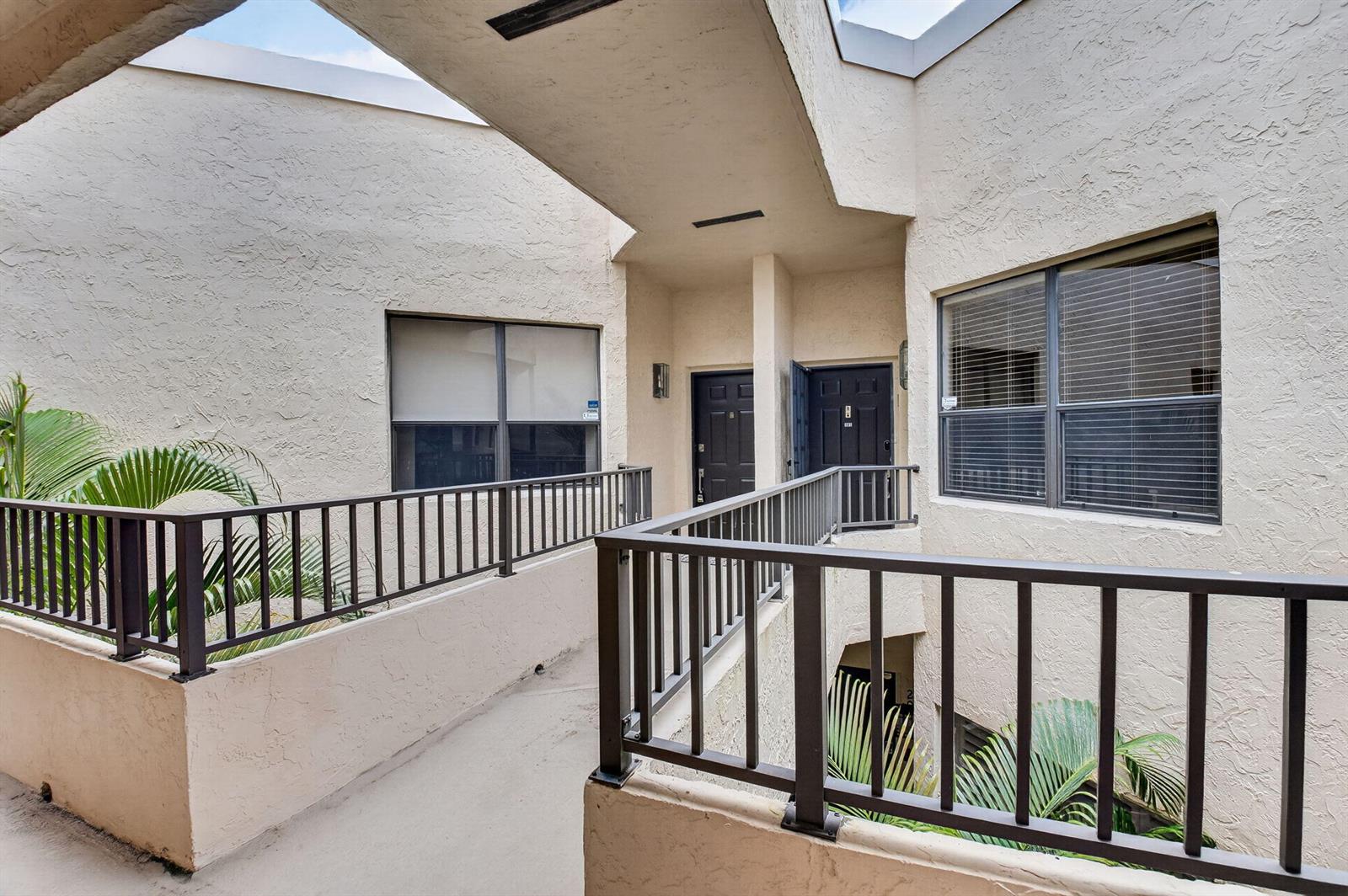 An outdoor walkway with metal railings connects two apartment entrances in a stucco building — 7460 La Paz Boulevard # 306, Boca Raton FL 33433, BOCA RATON, FL