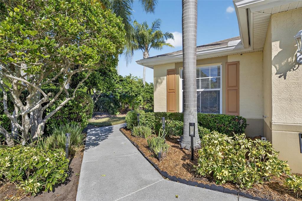 A concrete walkway leads to the front entrance of a house with tan stucco siding — 1201 CORINTH GREENS DRIVE UNIT 58, SUN CITY CENTER, FL