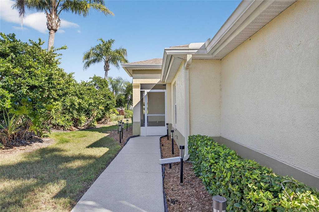 A concrete walkway leads to a screened entryway along the side of a stucco house — 1201 CORINTH GREENS DRIVE UNIT 58, SUN CITY CENTER, FL