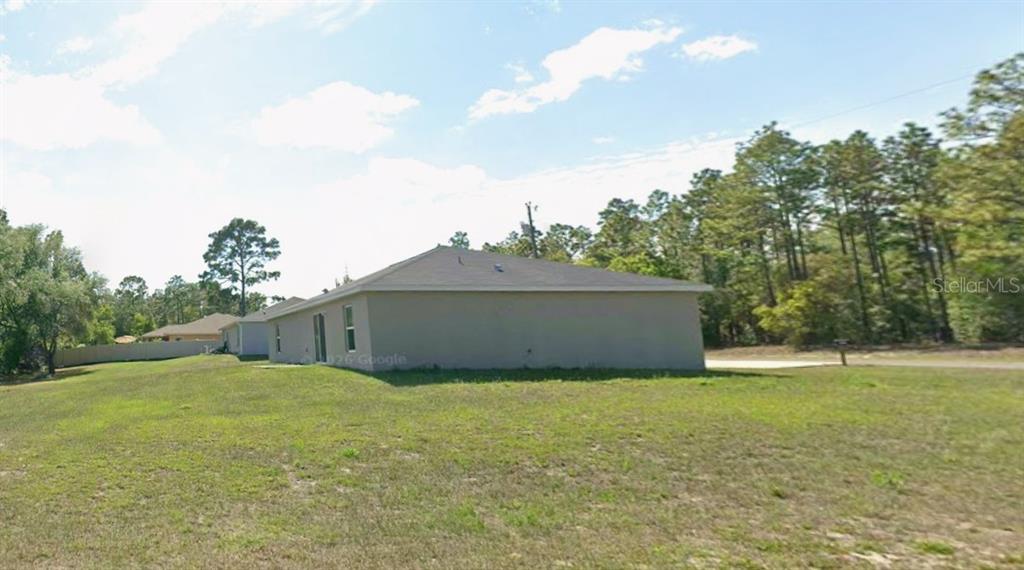 A side view of a single-story house with a beige stucco exterior and a yard — 1958 W LINDEN DRIVE, CITRUS SPRINGS, FL