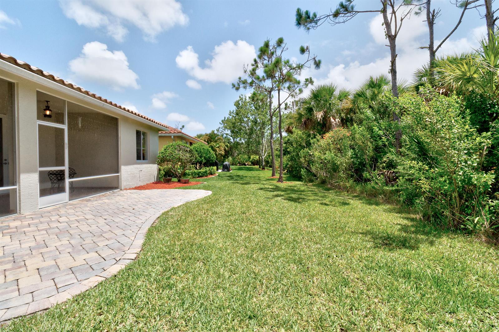 A paved patio extends from a screened-in porch into a grassy backyard with lush landscaping — 6188 Dorchester Way, Vero Beach FL 32966, VERO BEACH, FL