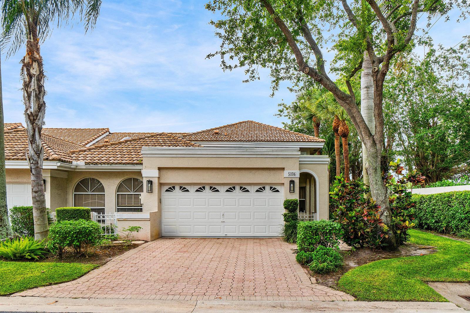 A beige single-story house features a white garage door, arched windows, and a paved driveway — 5106 Windsor Parke Drive, Boca Raton FL 33496, BOCA RATON, FL