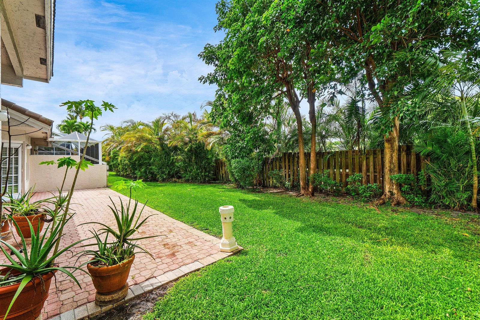 A paved patio overlooks a grassy backyard with mature trees and a wooden privacy fence — 5106 Windsor Parke Drive, Boca Raton FL 33496, BOCA RATON, FL