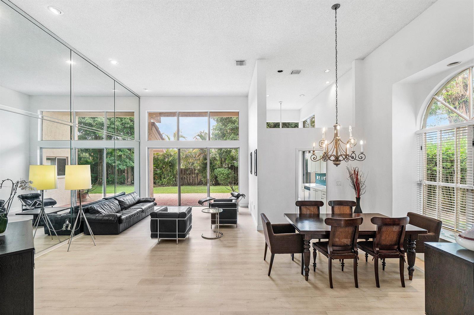 A spacious living and dining area with light wood floors, floor-to-ceiling mirrors, and large windows — 5106 Windsor Parke Drive, Boca Raton FL 33496, BOCA RATON, FL