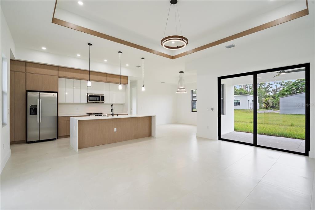 A modern kitchen and living area with light wood cabinetry, white countertops, and sliding glass doors — 17328 ORION AVENUE, PORT CHARLOTTE, FL