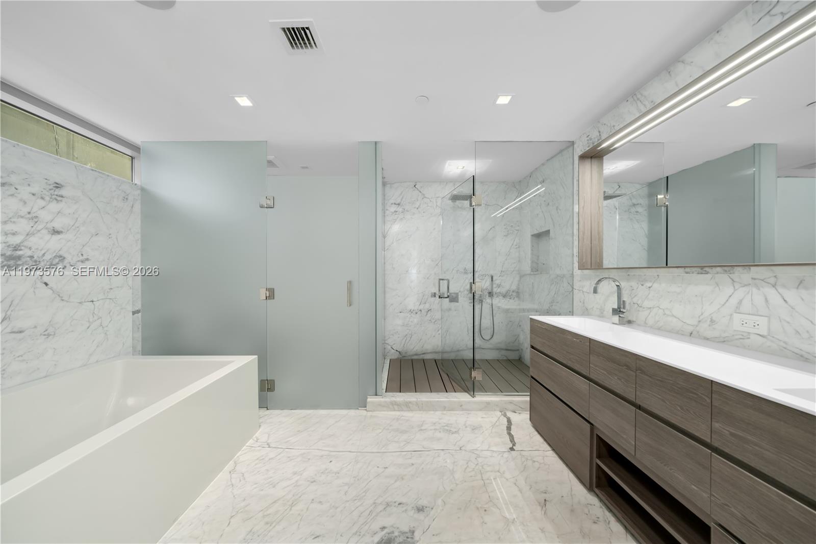 A modern bathroom features marble walls and flooring, a glass shower, and a wooden vanity — 321 Ocean Dr # 200, Miami Beach FL 33139, MIAMI BEACH, FL