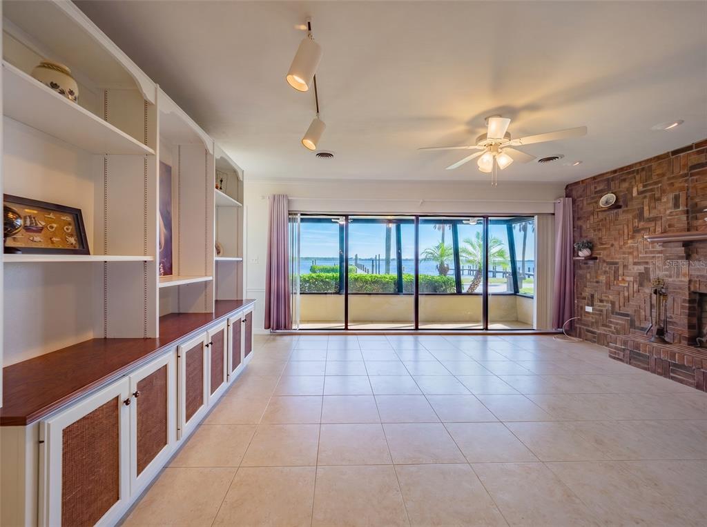 A living room features built-in shelving, a brick fireplace, tile flooring, and large sliding glass doors — 2410 RIVERSIDE DRIVE E, BRADENTON, FL