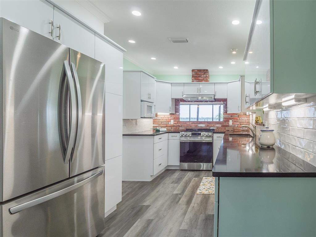 A modern kitchen features white cabinetry, stainless steel appliances, dark countertops, and a brick backsplash — 2410 RIVERSIDE DRIVE E, BRADENTON, FL