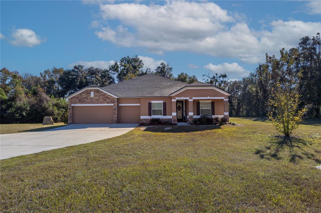 A single-story suburban house with a tan stucco exterior, stone accents, and a concrete driveway — 6075 SW 215TH TERRACE, NEWBERRY, FL
