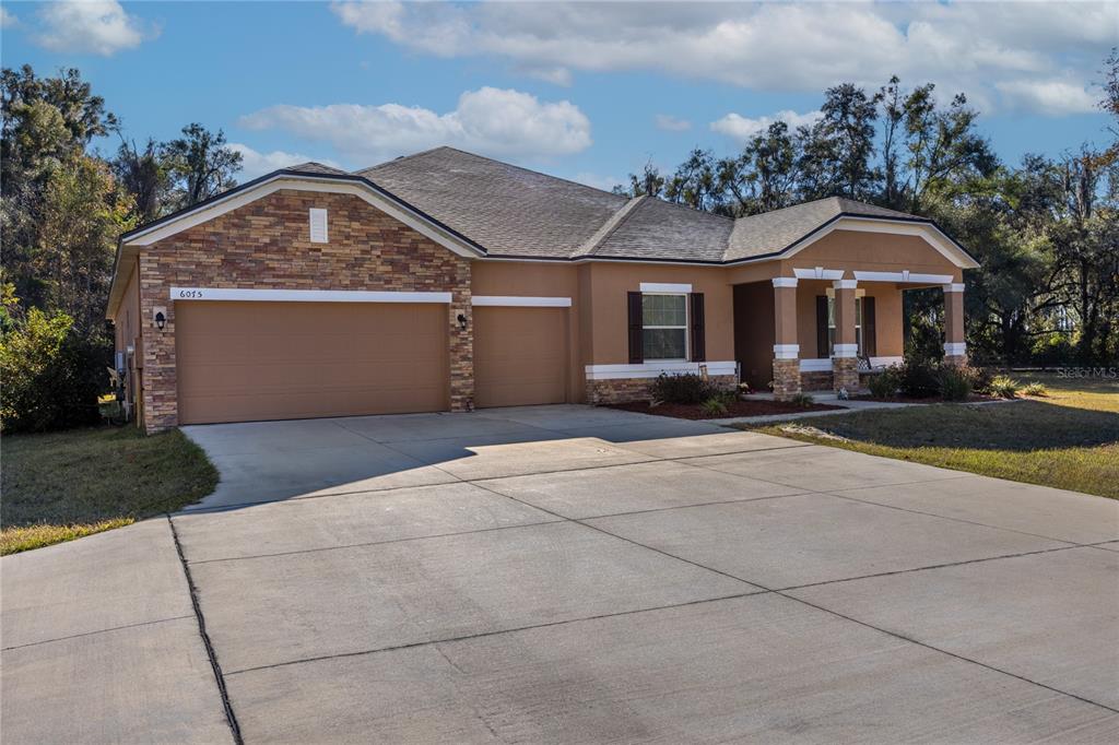 A single-story house with a stone-accented facade, a three-car garage, and a covered front porch — 6075 SW 215TH TERRACE, NEWBERRY, FL