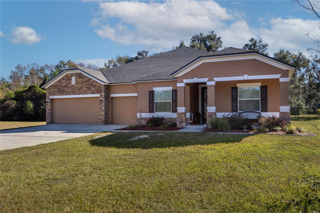 A single-story house with a tan stucco exterior, stone accents, and a three-car garage — 6075 SW 215TH TERRACE, NEWBERRY, FL