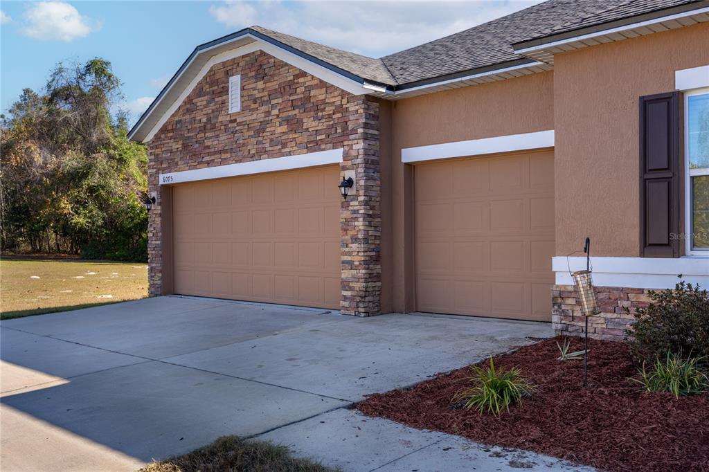 A tan house exterior features a two-car garage with stone veneer accents and a driveway — 6075 SW 215TH TERRACE, NEWBERRY, FL