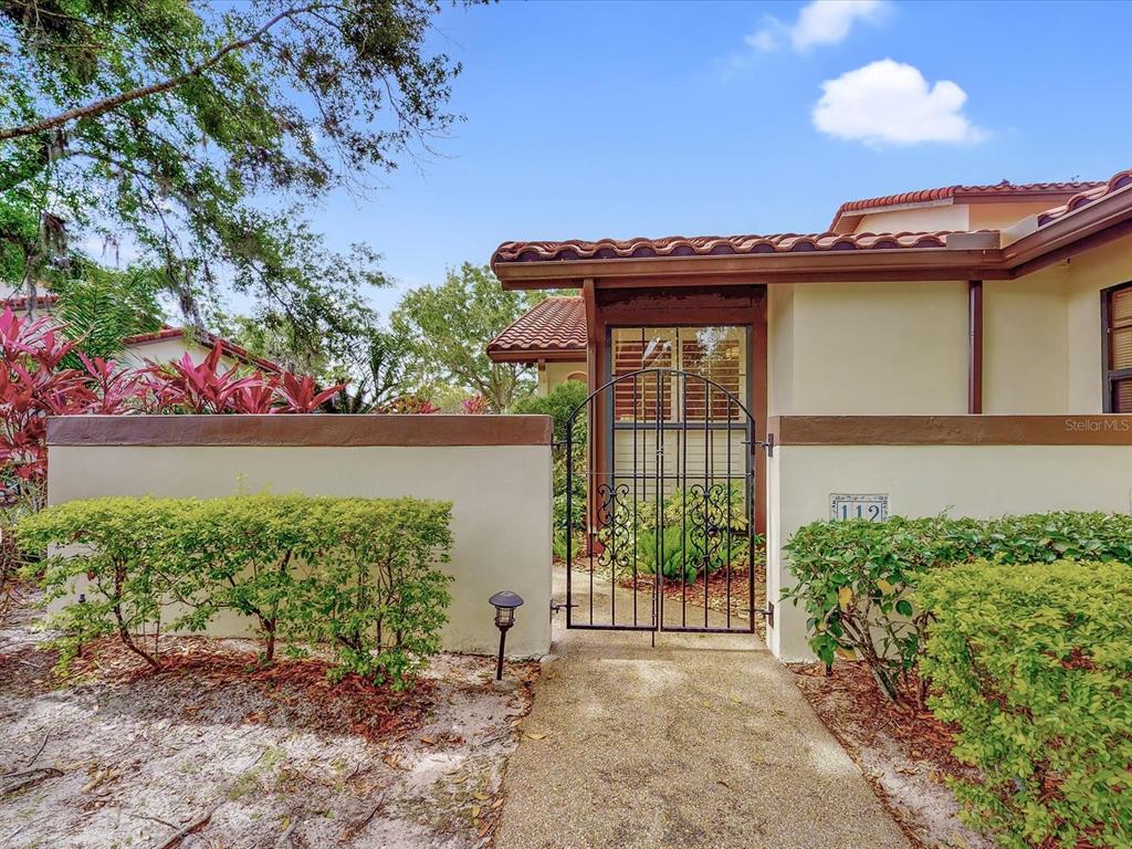 A concrete walkway leads to a gated courtyard entrance of a house with stucco walls — 112 COVENTRY LANE, HAINES CITY, FL