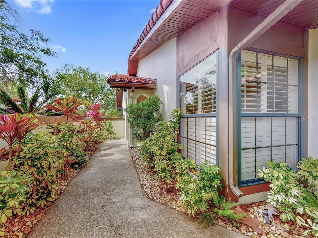 A concrete walkway leads past a house exterior with a window and tropical landscaping — 112 COVENTRY LANE, HAINES CITY, FL