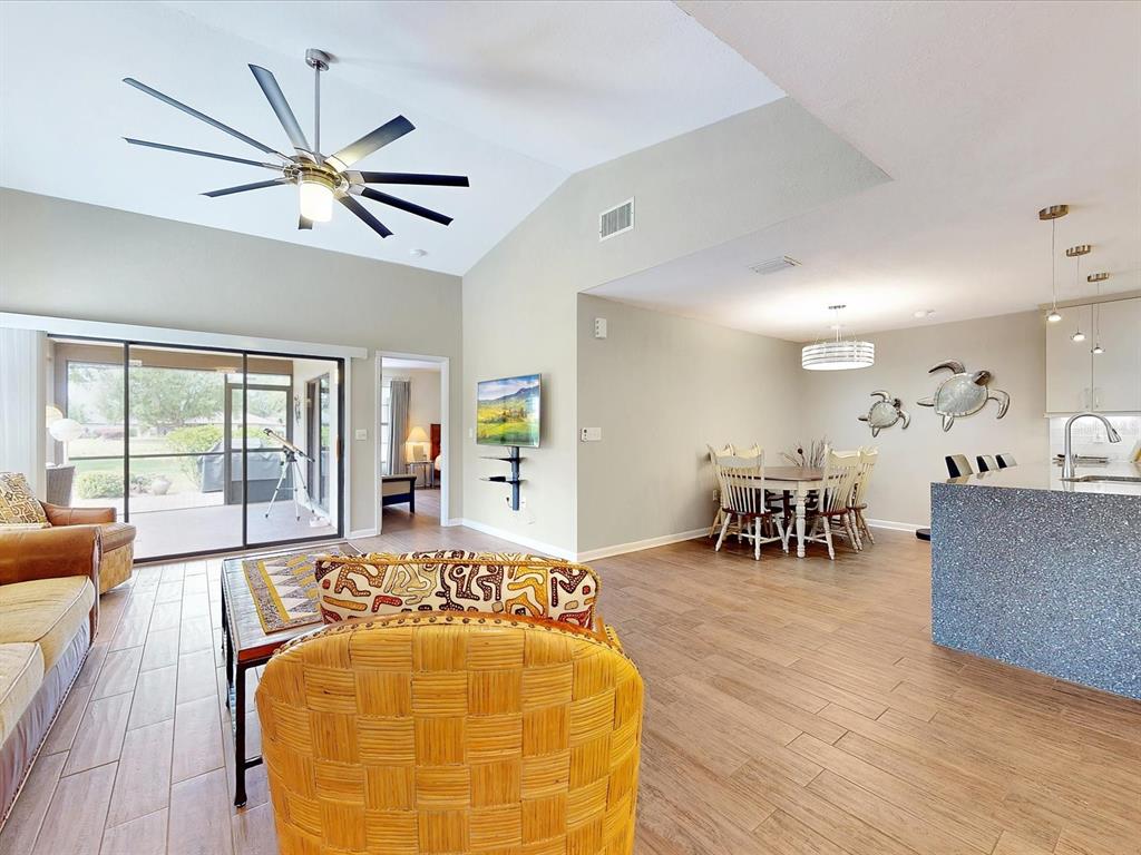 An open-concept living and dining area features wood-look tile flooring, a vaulted ceiling, and patio access — 112 COVENTRY LANE, HAINES CITY, FL