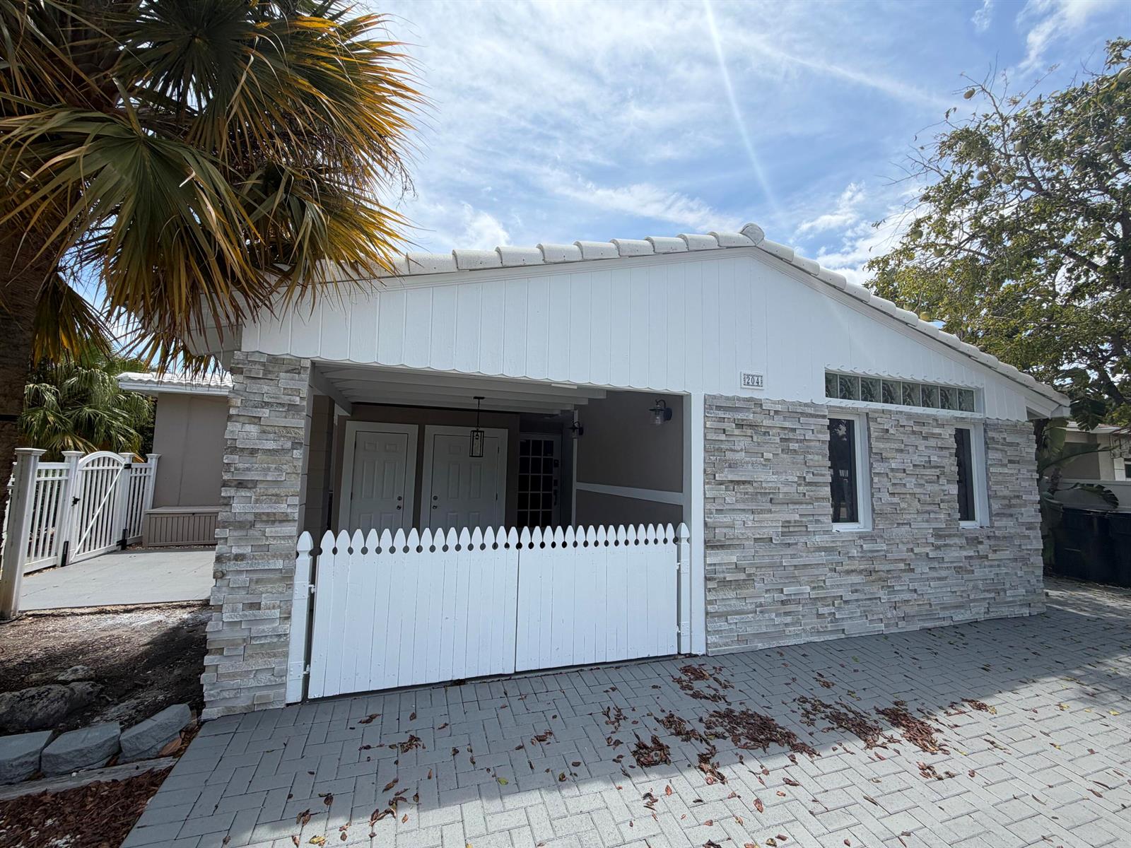 A single-story house exterior features white vertical siding, stone veneer, and a white picket gate — 204 S Seacrest Circle, Delray Beach FL 33444, DELRAY BEACH, FL