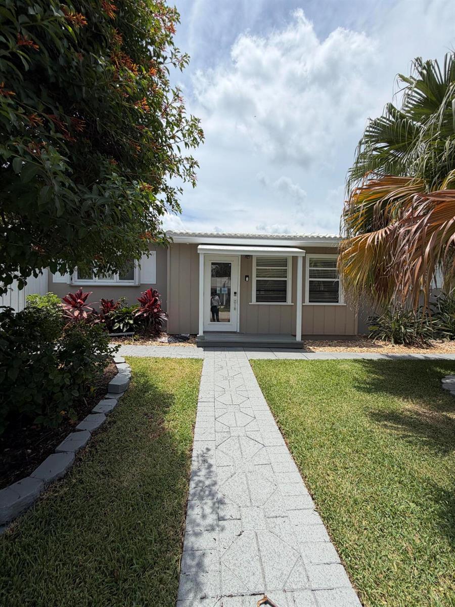 A paved walkway leads to the front entrance of a single-story home with tan siding — 204 S Seacrest Circle, Delray Beach FL 33444, DELRAY BEACH, FL