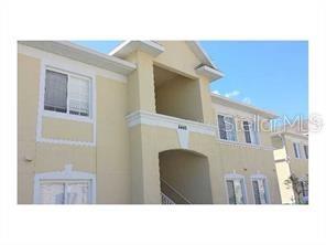 A low-angle exterior view of a multi-story, light yellow stucco apartment building under a blue sky — 6431 CYPRESSDALE DRIVE UNIT 202, RIVERVIEW, FL