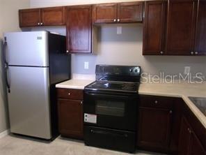 A kitchen features dark wood cabinets, a stainless steel refrigerator, and a black electric stove — 6431 CYPRESSDALE DRIVE UNIT 202, RIVERVIEW, FL