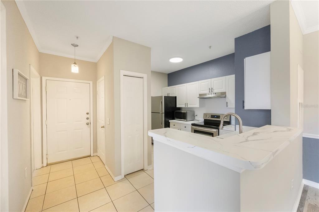 A kitchen with white cabinets and stainless steel appliances overlooks a tiled entryway — 18001 RICHMOND PLACE DRIVE UNIT 1010, TAMPA, FL