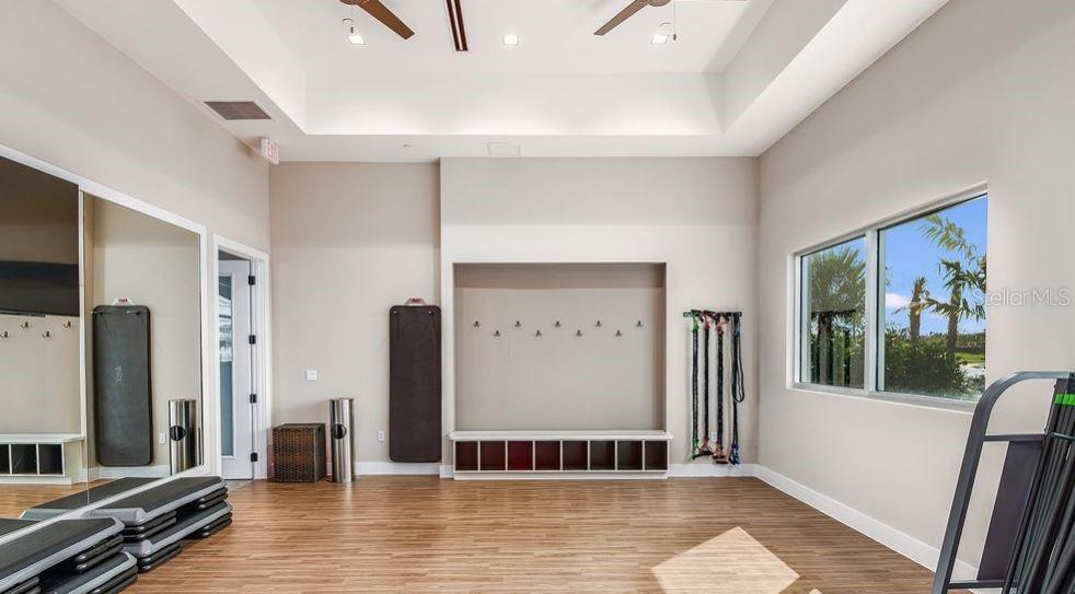 A fitness room with wood-look flooring, mirrored walls, a storage bench, and a large window — 4451 OCHOS RIOS PLACE, KISSIMMEE, FL