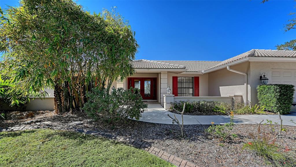 A single-story house with a beige exterior, red front doors, and a large bamboo tree — 1109 DELACROIX CIRCLE, NOKOMIS, FL