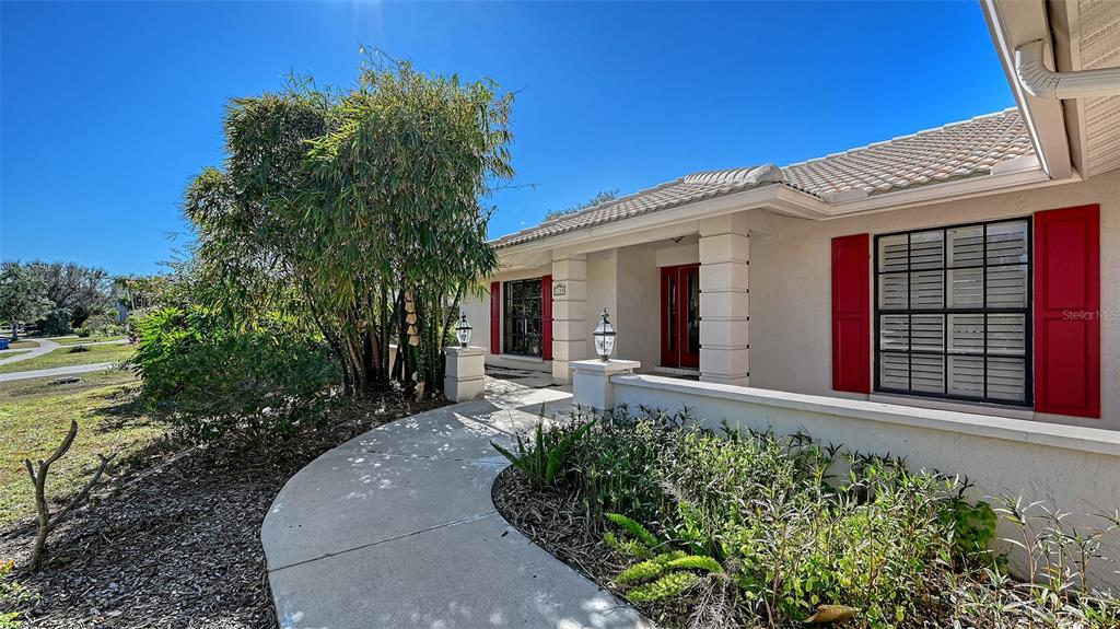 A concrete walkway leads to the front entrance of a house with red shutters — 1109 DELACROIX CIRCLE, NOKOMIS, FL