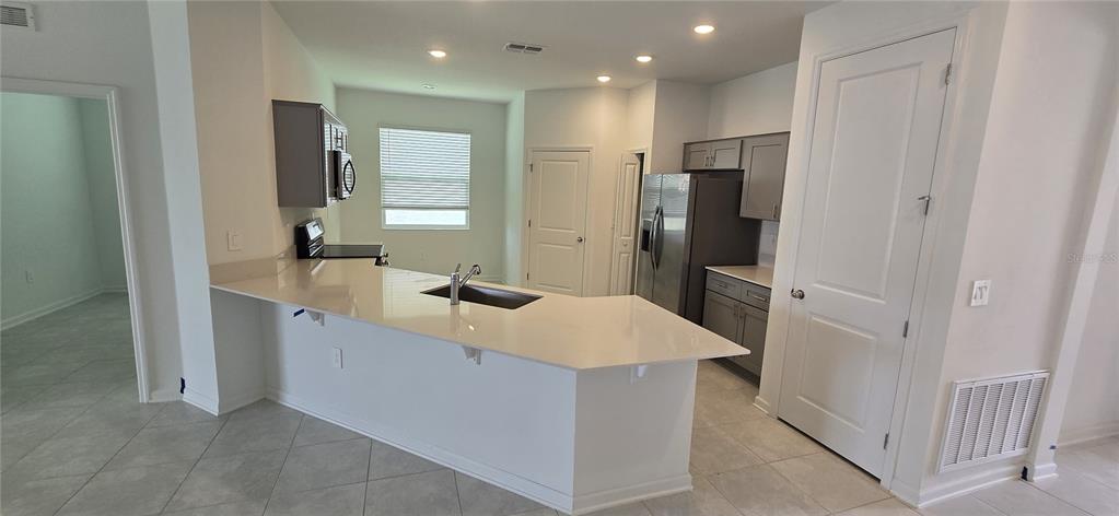 A kitchen features a white countertop island with a sink, gray cabinets, and stainless appliances — 1433 DEEPWATER CIR UNIT A, EAGLE LAKE, FL
