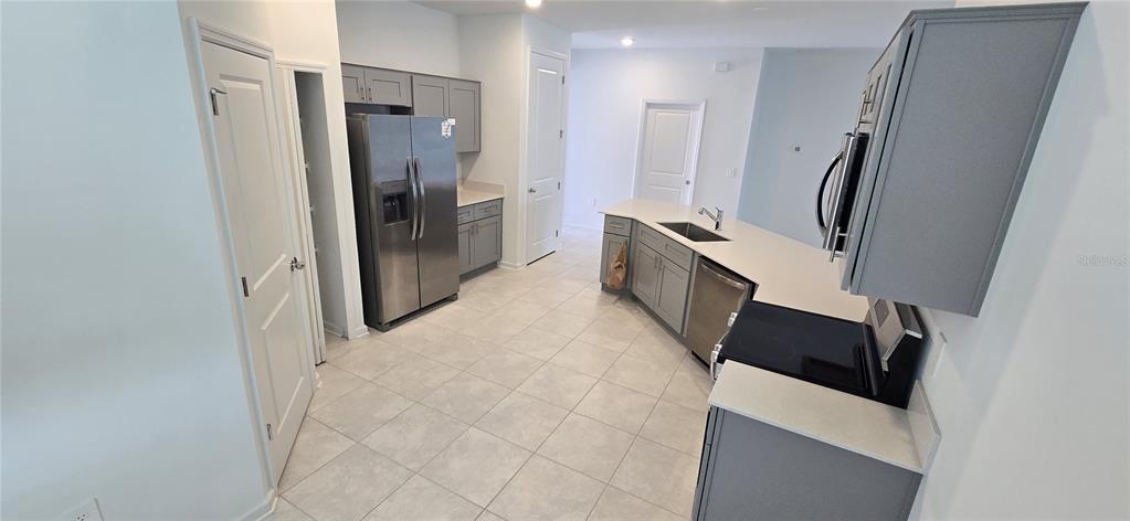 A kitchen features grey cabinets, stainless steel appliances, and light-colored tile flooring — 1433 DEEPWATER CIR UNIT A, EAGLE LAKE, FL