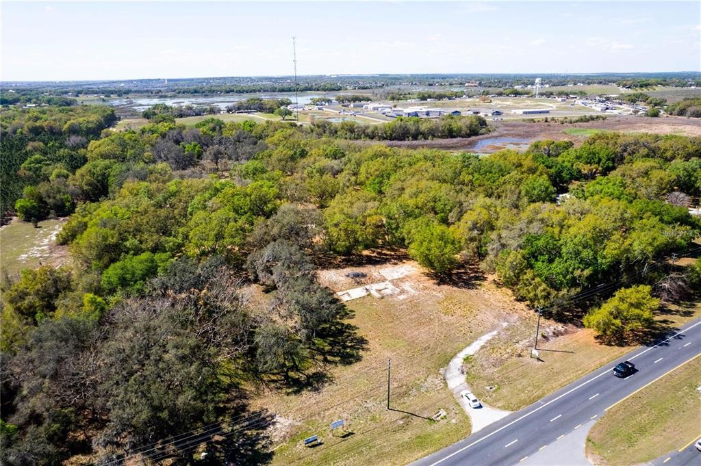 An aerial view shows a vacant, wooded lot with a concrete foundation beside a road — 18537 US HIGHWAY 27, MINNEOLA, FL