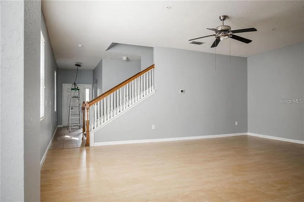 A living room with light wood flooring, gray walls, a ceiling fan, and a staircase — 14244 TURNING LEAF DRIVE, ORLANDO, FL