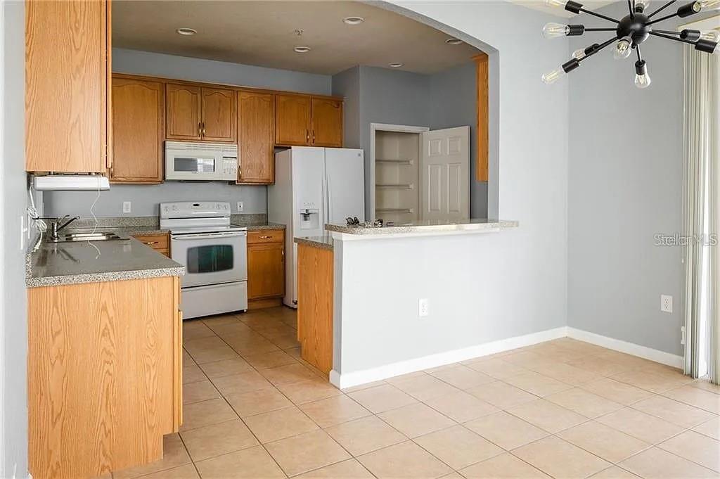 A kitchen with wood cabinets, white appliances, and a breakfast bar opens to a dining area — 14244 TURNING LEAF DRIVE, ORLANDO, FL