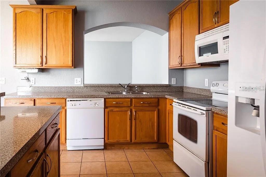 A kitchen features wood cabinets, granite countertops, white appliances, and a tiled floor — 14244 TURNING LEAF DRIVE, ORLANDO, FL