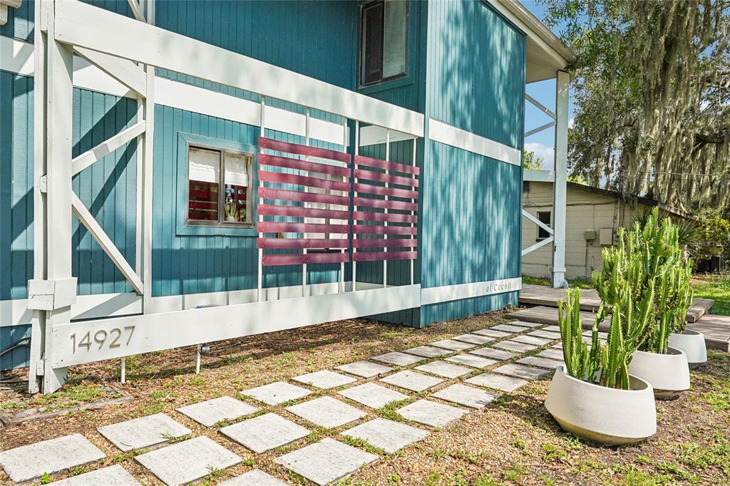 A blue house exterior features a white trellis, a stone paver walkway, and potted cacti — 14927 HARDY DRIVE W, TAMPA, FL