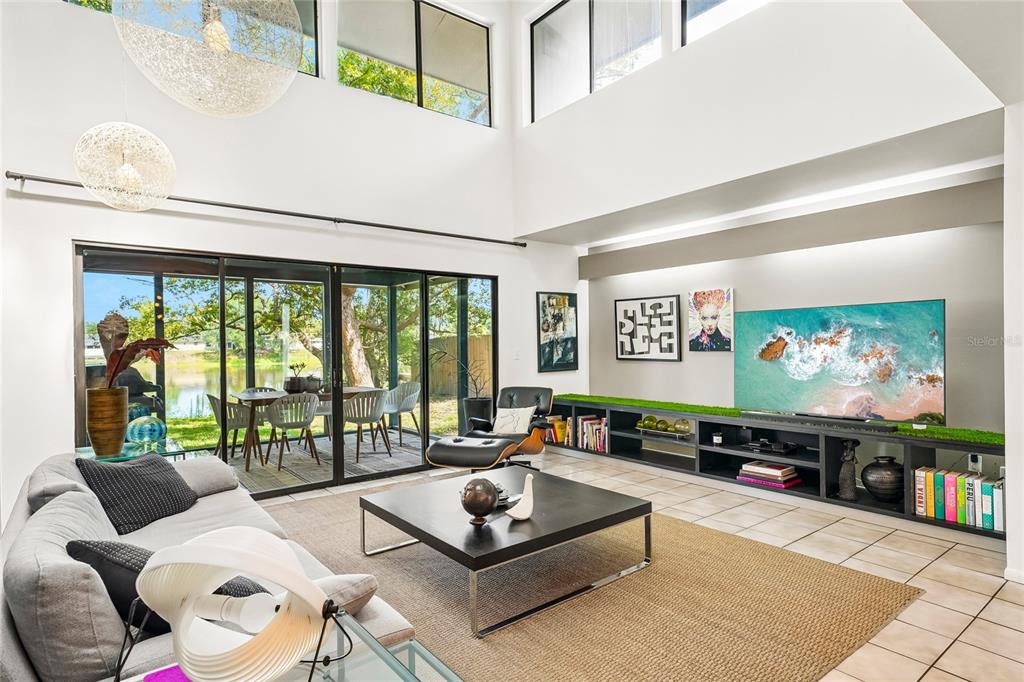 A bright living room features a high ceiling, tile floors, and a view of a lake — 14927 HARDY DRIVE W, TAMPA, FL