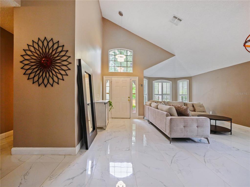 A living room with vaulted ceilings, white marble tile floors, and a beige sectional sofa — 4944 NATIVE DANCER LANE, ORLANDO, FL