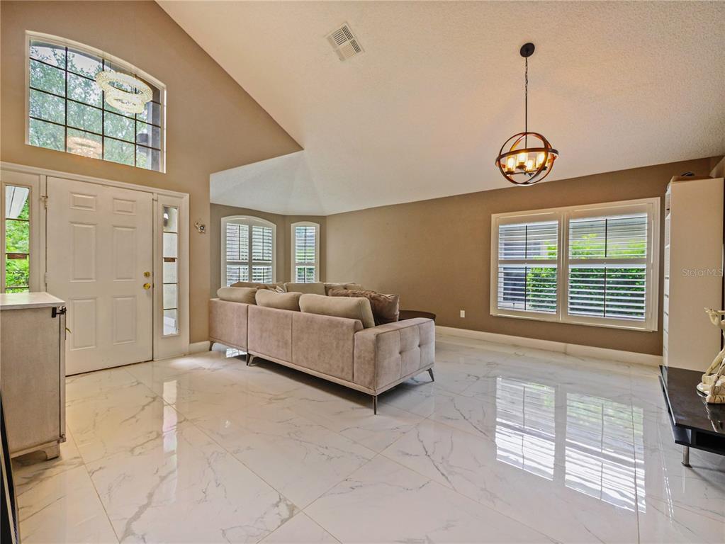 A living room with white marble floors, a beige sofa, and a vaulted ceiling — 4944 NATIVE DANCER LANE, ORLANDO, FL