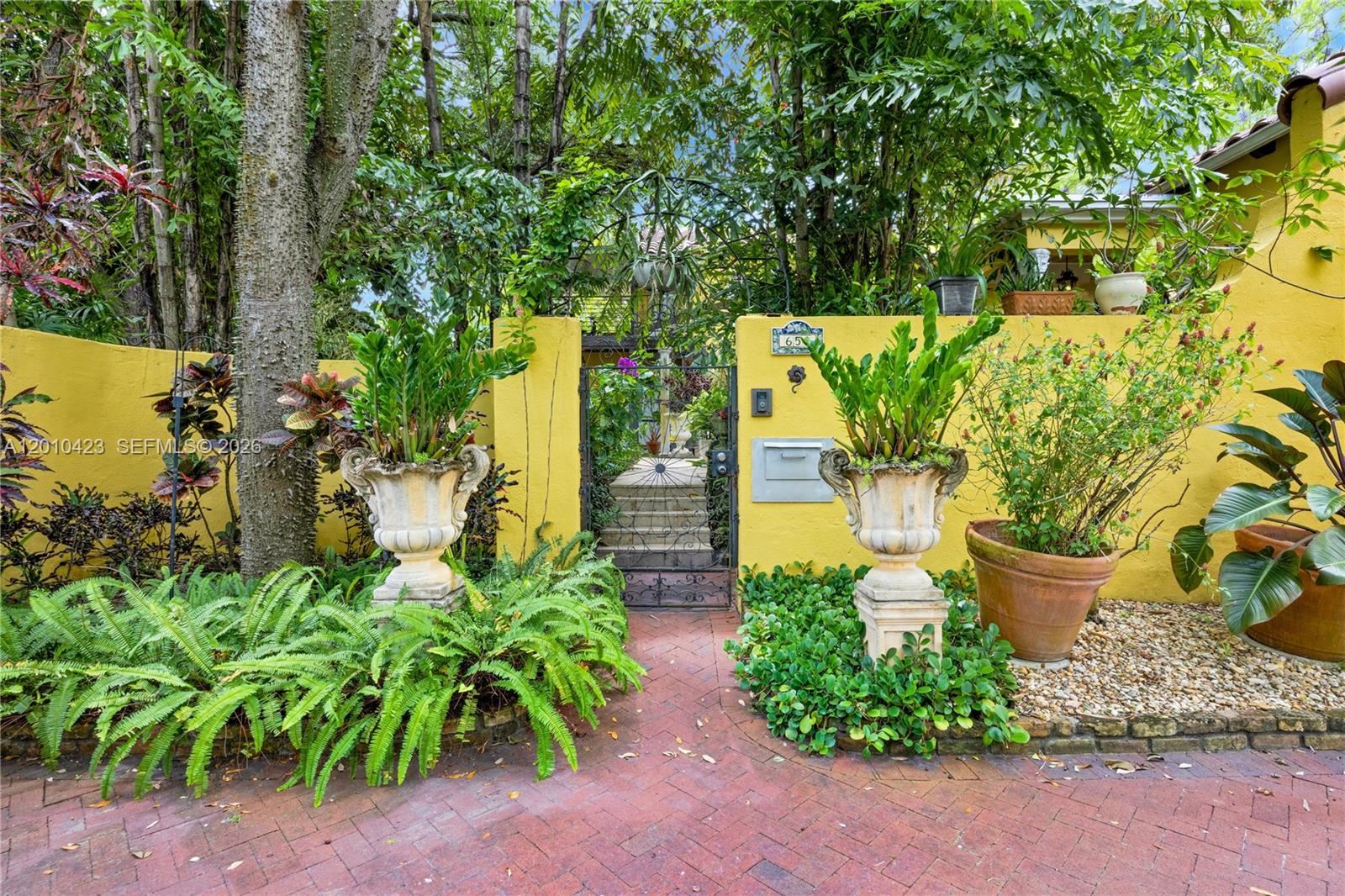 A brick walkway leads to a gated entrance in a yellow wall with potted plants — 650 NE 76th St, Miami FL 33138, MIAMI, FL