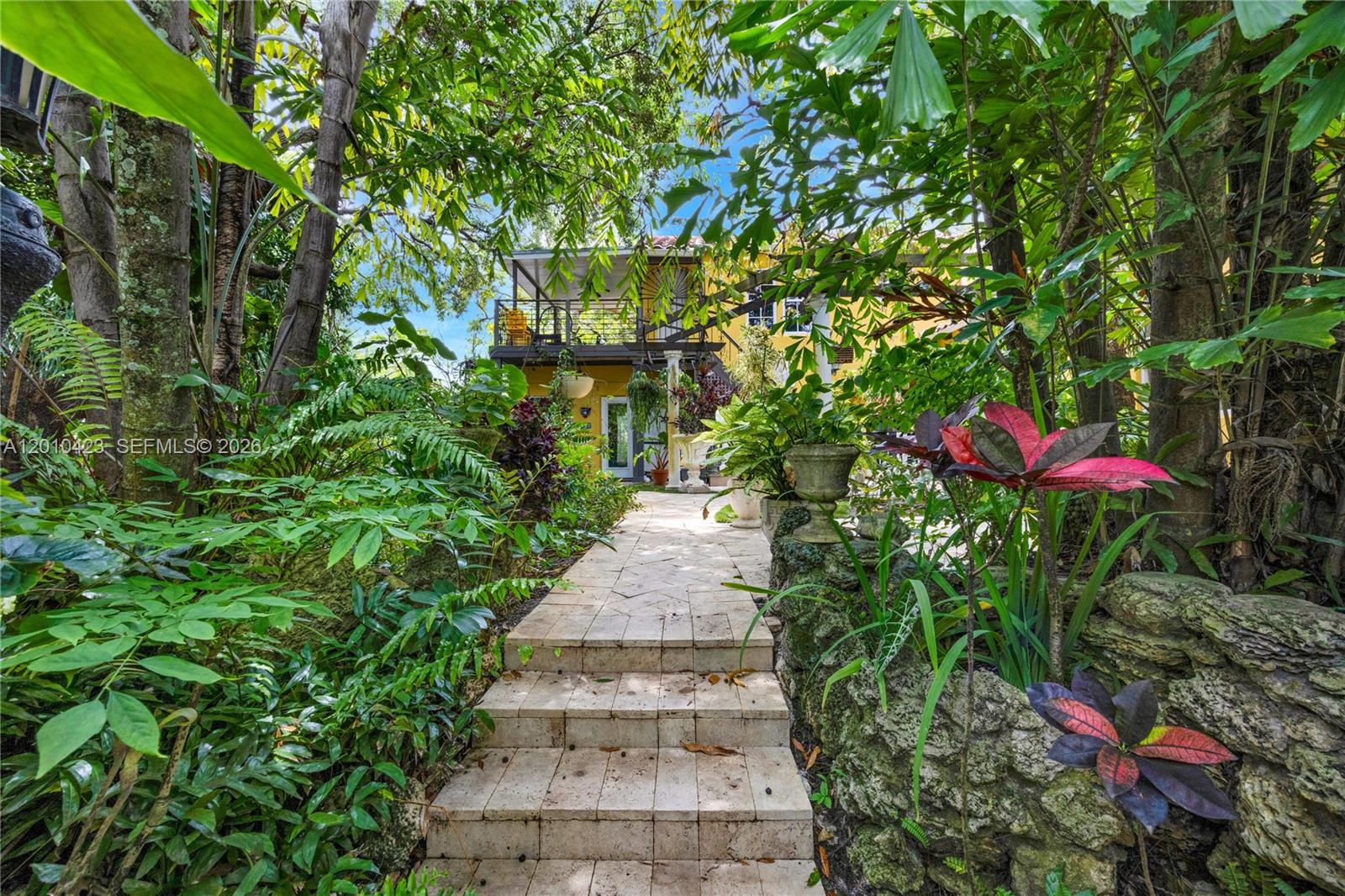 A stone staircase leads through a lush garden toward a yellow house with a balcony — 650 NE 76th St, Miami FL 33138, MIAMI, FL